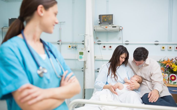 Doctor crossing her arms with a family Doctor crossing her arms in the foreground of a room with a family with a baby in a hospital room